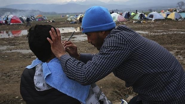 Un refugiado afeita a su compañero en el campamento provisional de Idomeni, en la frontera entre Grecia y Macedonia, hoy, 17 de marzo de 2016