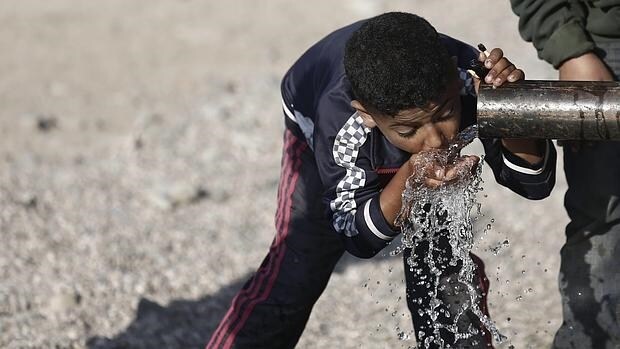 Un niño refugiado toma agua de una tubería en un campo de refugiados en Grecia