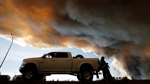 Varios ciudadanos esperan junto a un control de carretera, mientras el humo se eleva al fondo