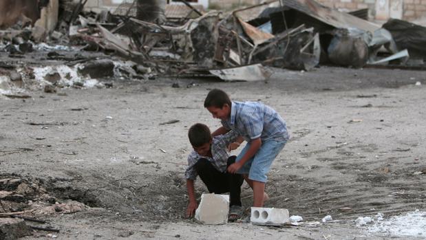 Dos niños juegan en un lugar donde cayó una bomba el sábado en Hasaka, Siria