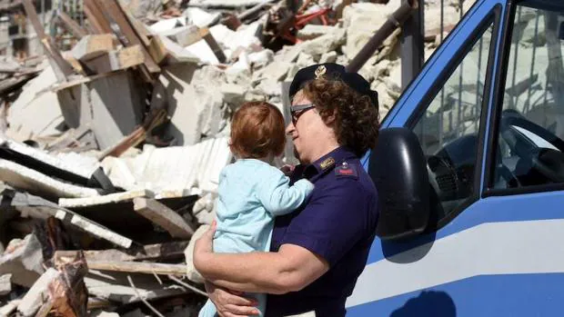 Una agente de policía lleva en brazos a un bebé cerca de los escombros de varios edificios en Pescara del Tronto