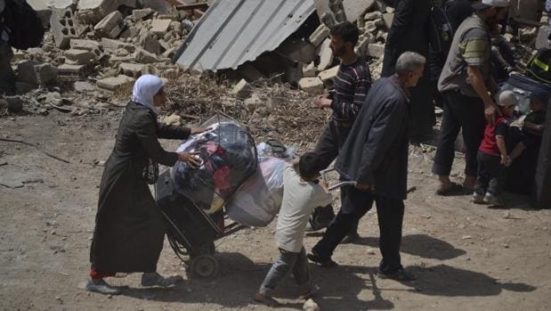 Varias familias portan sus pertenencias mientras abandonan la ciudad de Daraya, en el suroeste de Damasco bajo la supervisión de la ONU y la Media Luna Roja Siria