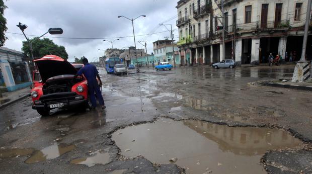 Un hombre intenta reparar su vehículo en una calle de La Habana mientras llueve