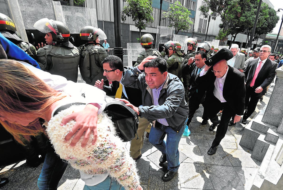 Diputados de la oposición se protegen al entrar ayer en el Parlamento asediado por militantes chavistas