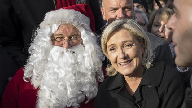 La líder del ultraderechista Frente Nacional (FN) francés, Marine Le Pen (d), posa junto a un papá noel durante una visita a un mercado navideño en los Campos Elíseos en París