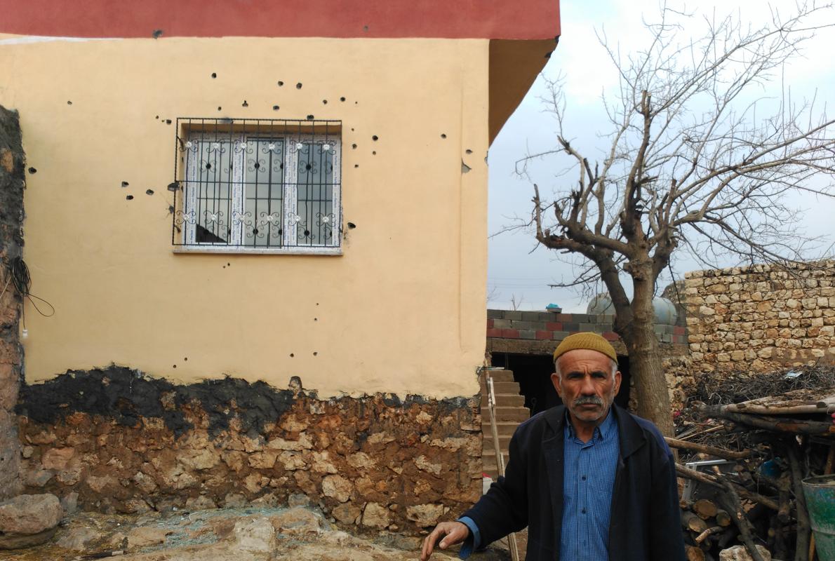 Uno de los habitantes de Korukoy, junto a una fachada llena de balazos