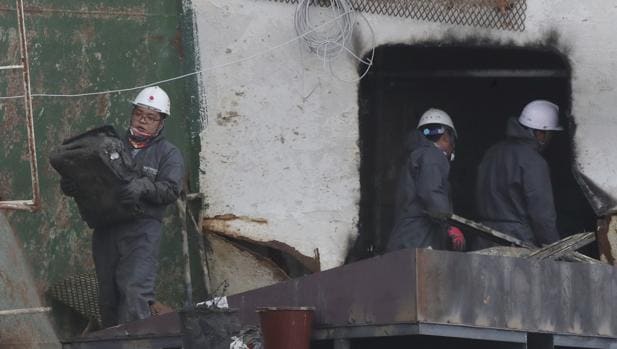Un operario carga con una maleta recuperada del interior del ferri hundido Sewol después de que fuera remolcado a dique seco