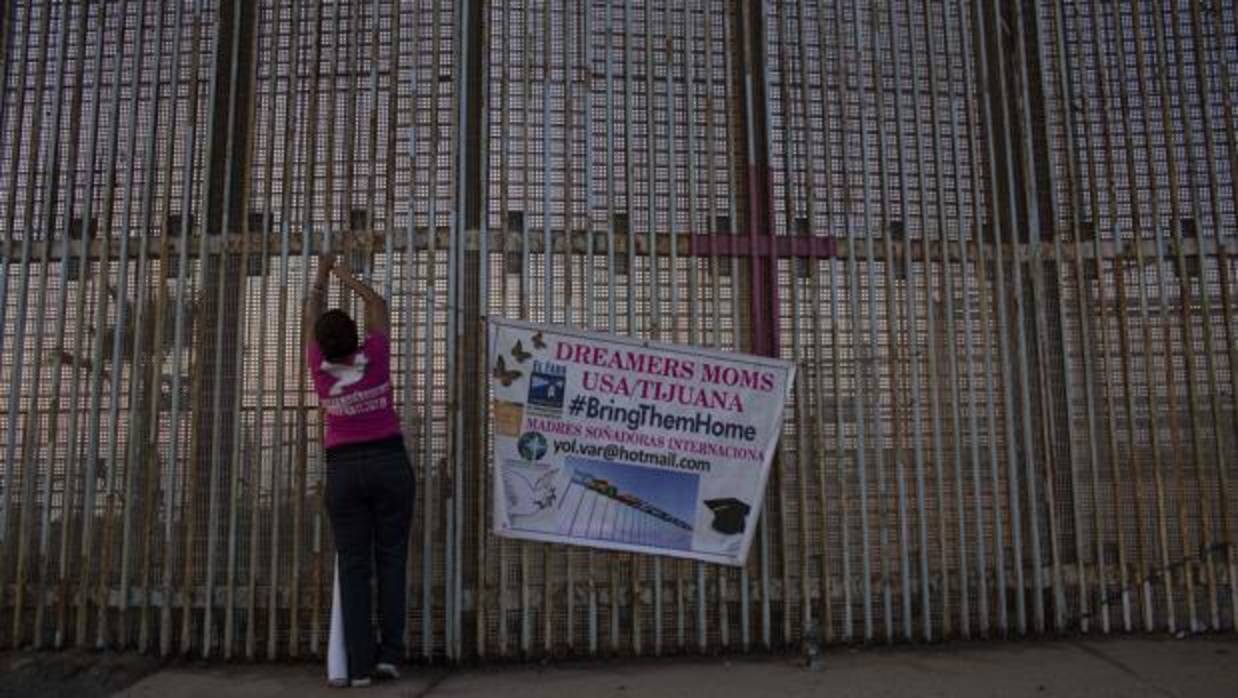 Una mujer cuelga una pancarta en la pared entre México y Estados Unidos durante una protesta contra el fin del programa DACA en Playas de Tijuana, Baja California