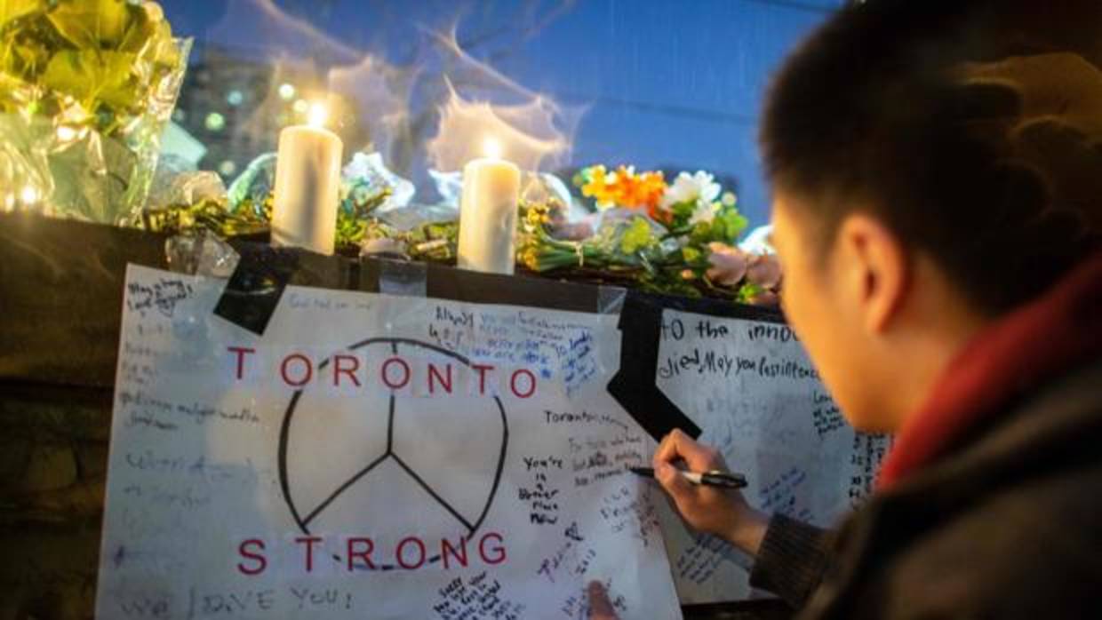 Un joven escribe un mensaje junto a unsímbolo de paz, durante una vigiia por las víctimas de Toronto