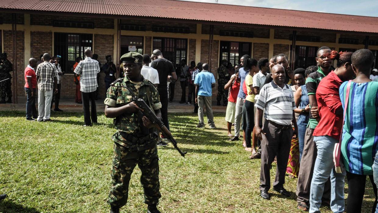 Un guardia de seguridad se encuentra junto a los votantes haciendo cola para votar fuera de un colegio electoral en Bujumbura