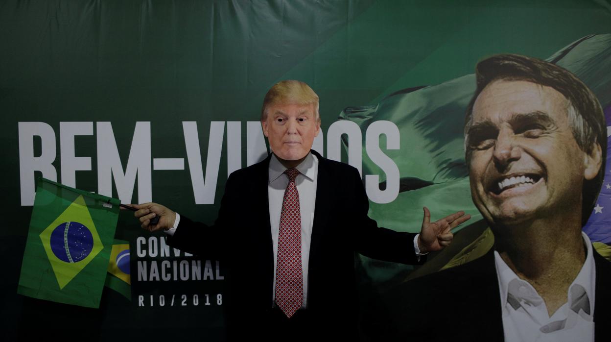Un seguiidor de Bolsonaro usa una máscara de Trump junto a un cartel electoral del candidato brasileño