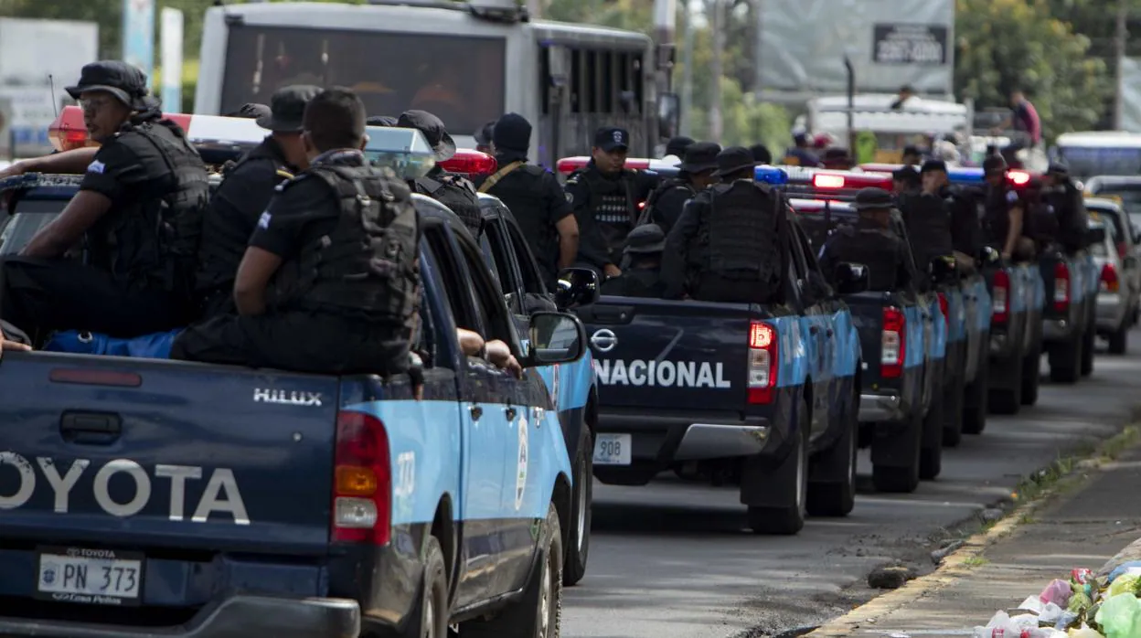Varias patrullas de policías pasan frente a jóvenes con banderas de Nicaragua que participan en un plantón