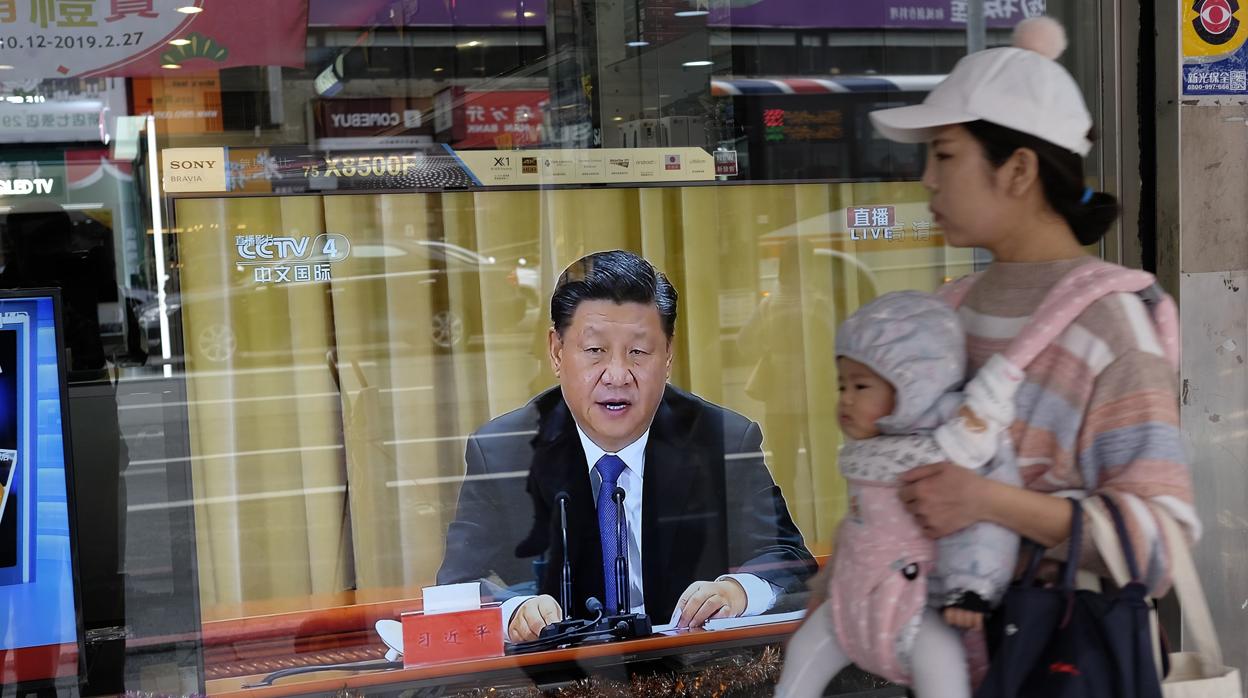 Una mujer pasa, con su hijo, por delante de una tienda de televisores en Taipei durante el discurso del presidente Xi