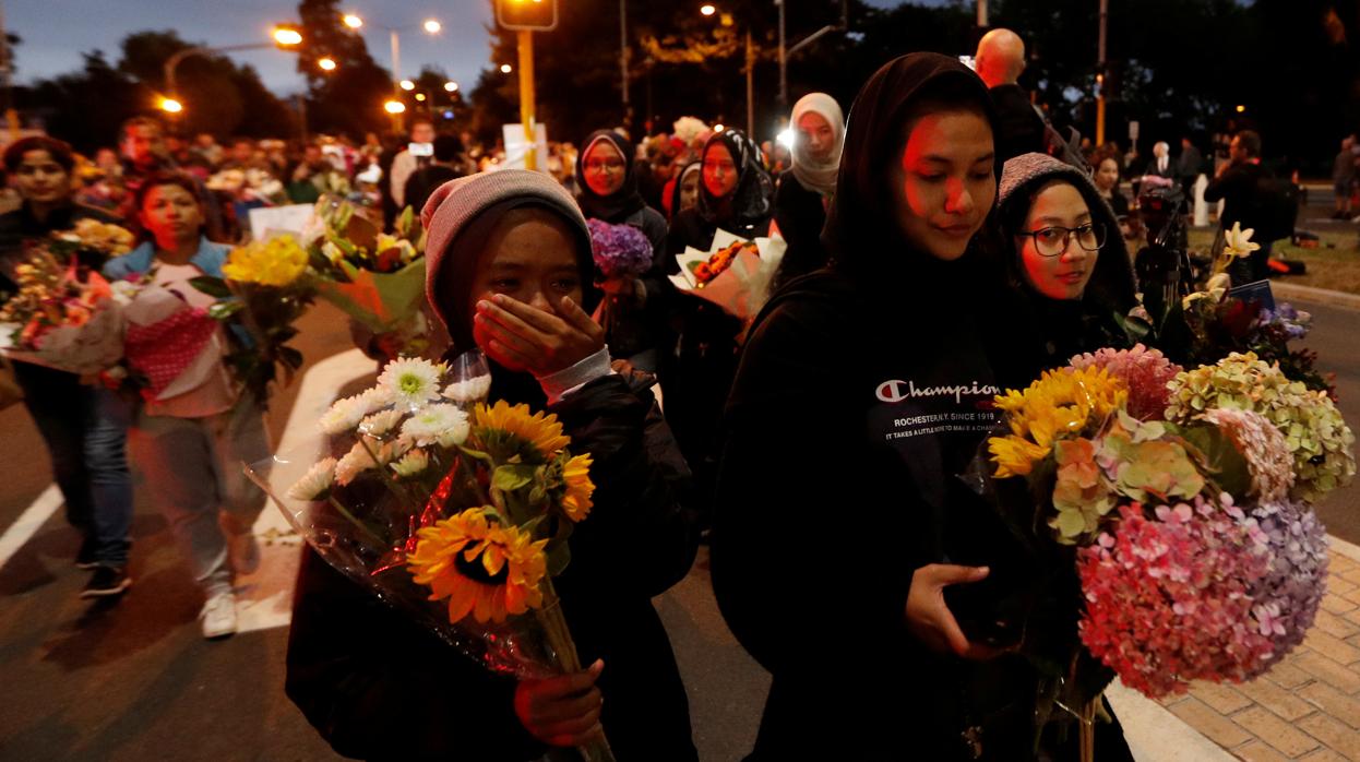 Un grupo de personas con flores avanza tras retirarse un cordón policial frente a la mezquita Al Noor