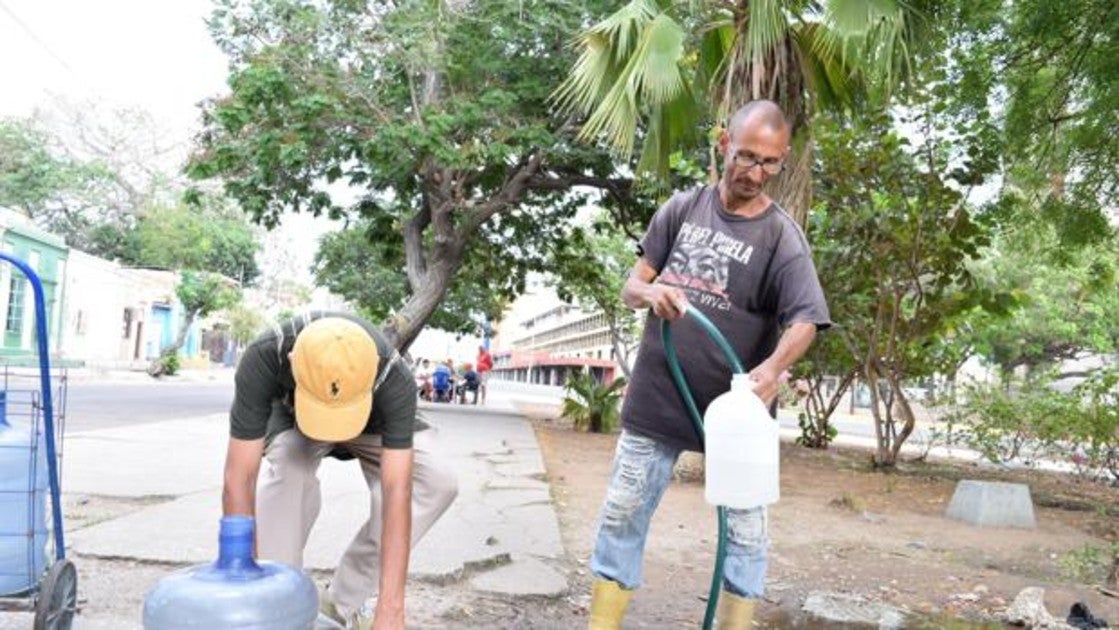 Dos venezolanos llenan bidones con agua en la calle en Maracaibo