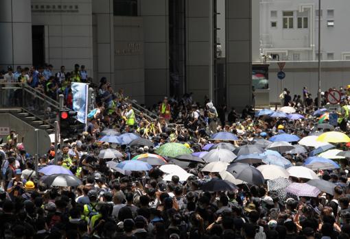 Con camisetas negras, máscaras y paraguas, varios millares de jóvenes y adolescentes rodean la comisaría central de Wan Chai, en Hong Kong