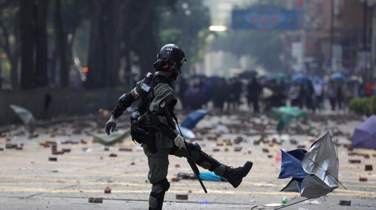 Un policía antidisturbios patea un paraguas, símbolo de la revolución hongkonesa