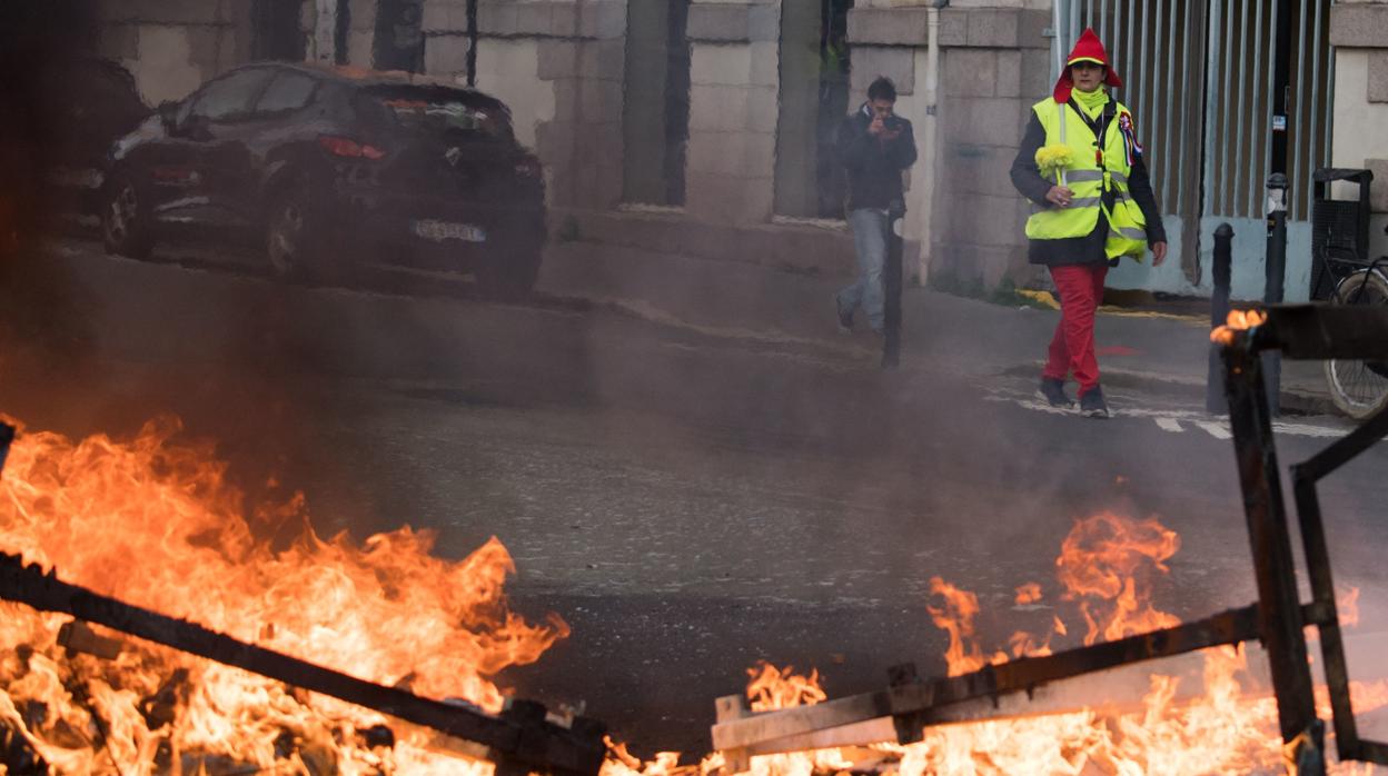 Un chaleco amarillo camina ante una barricada de fuego en París