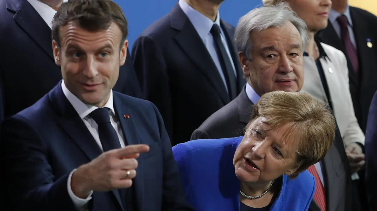 La canciller, Angela Merkel, asoma la cabeza entre Emmanuel Macron y António Guterres