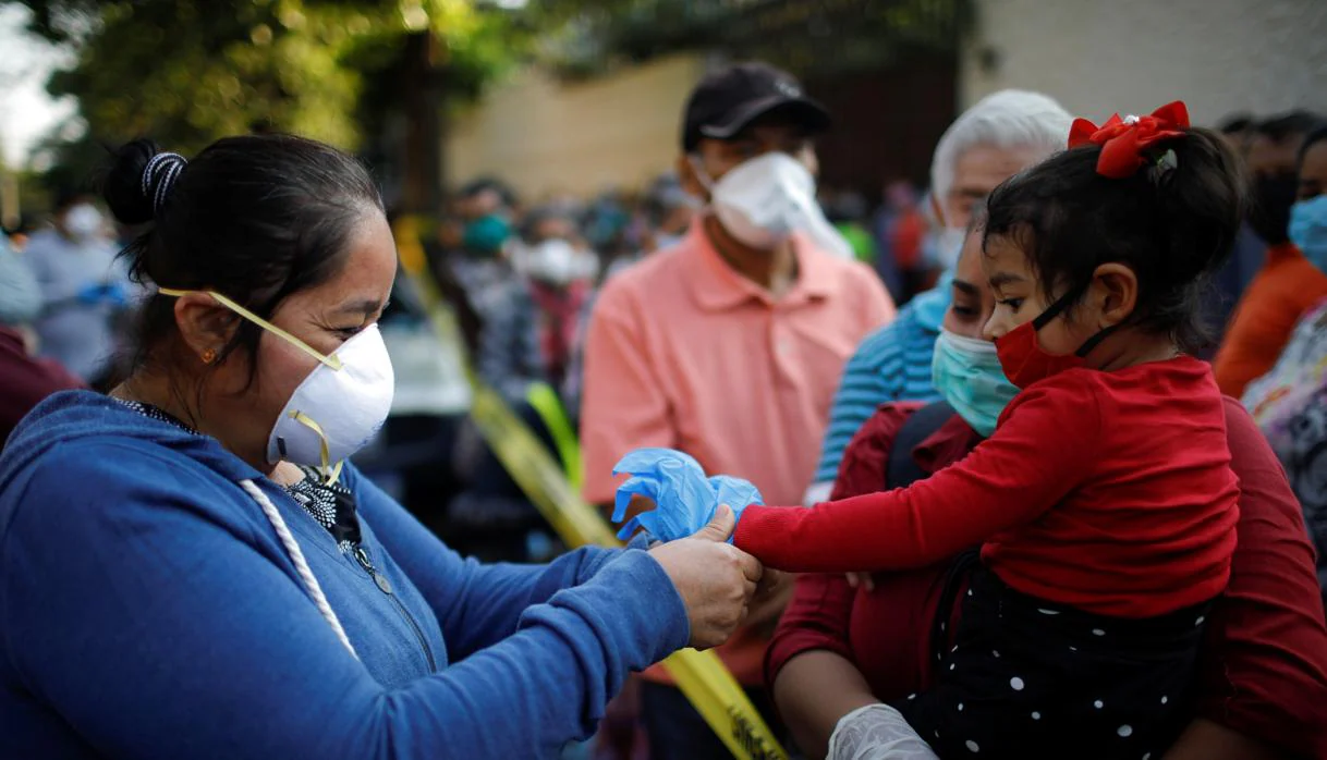 Una mujer intenta poner unos guantes a un niña, en San Salvador