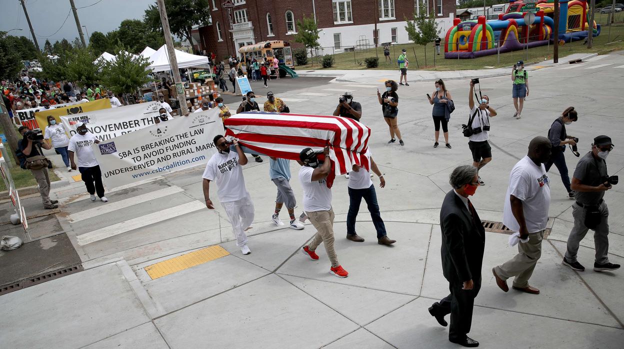 Un grupo de personas portan un ataúd envuelto en la bandera de EE.UU. que simboliza la destrucción del Wall Street negro de Tulsa (Oklahoma)en 1921