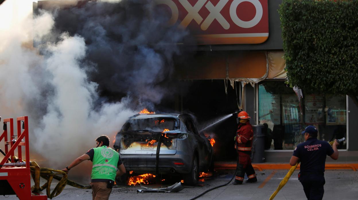 Los bomberos intentan apagar un incendio de un coche tras una operación contra el crimen organizado en Celaya