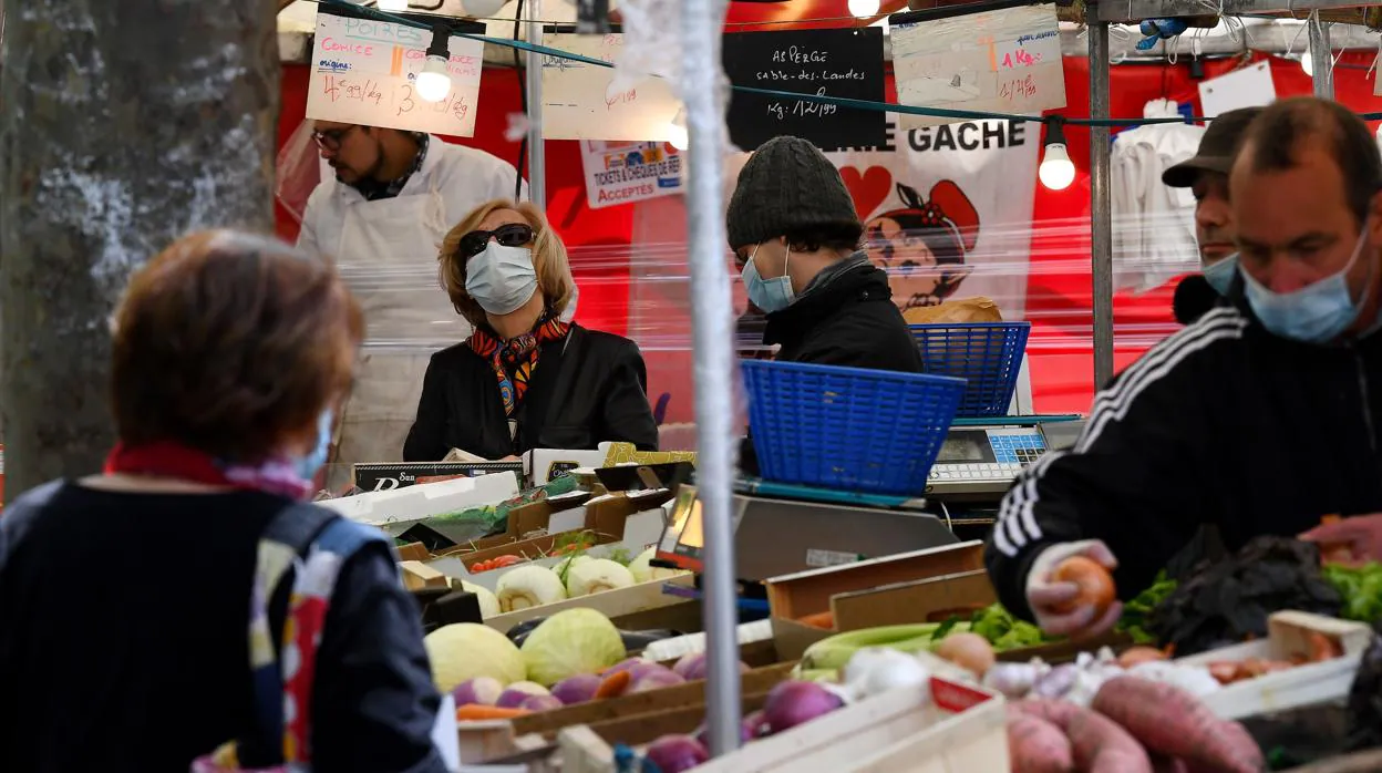 Una mujer lleva mascarilla para hacer la compra de verduras en un mercado del distrito de París