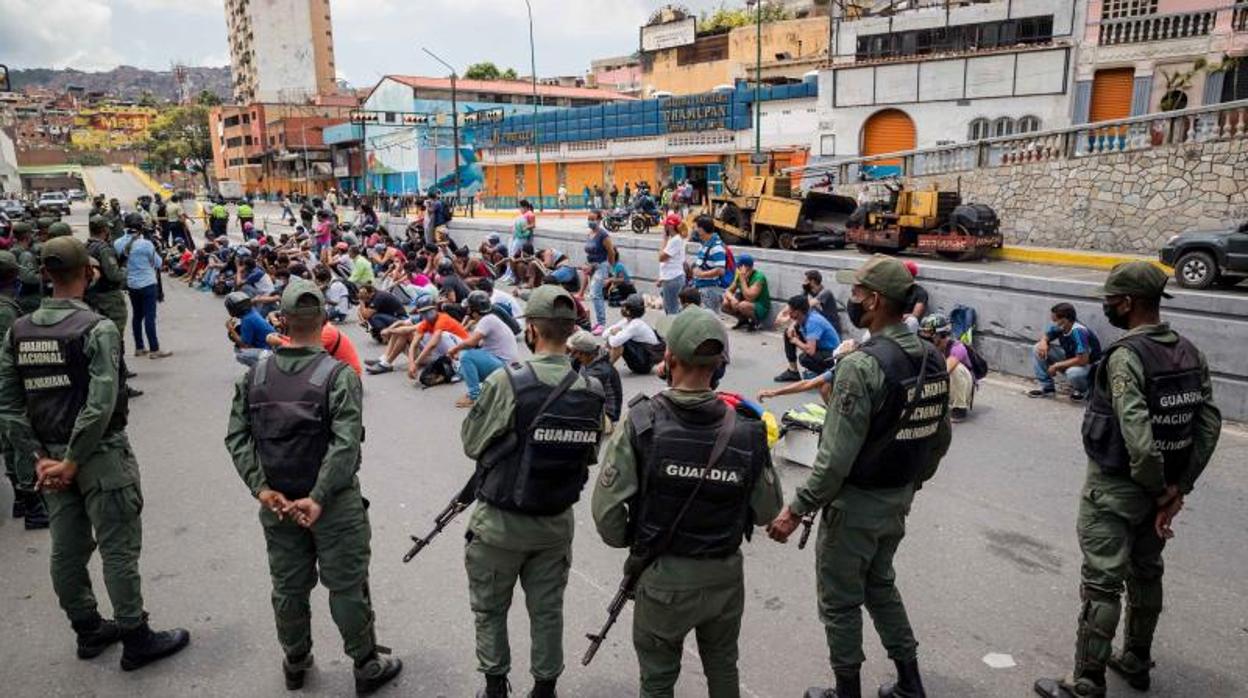 Miembros de la Guardia Nacional Bolivariana custodian a un grupo de personas retenidas por incumplir normativas para frenar la aceleración de la pandemia