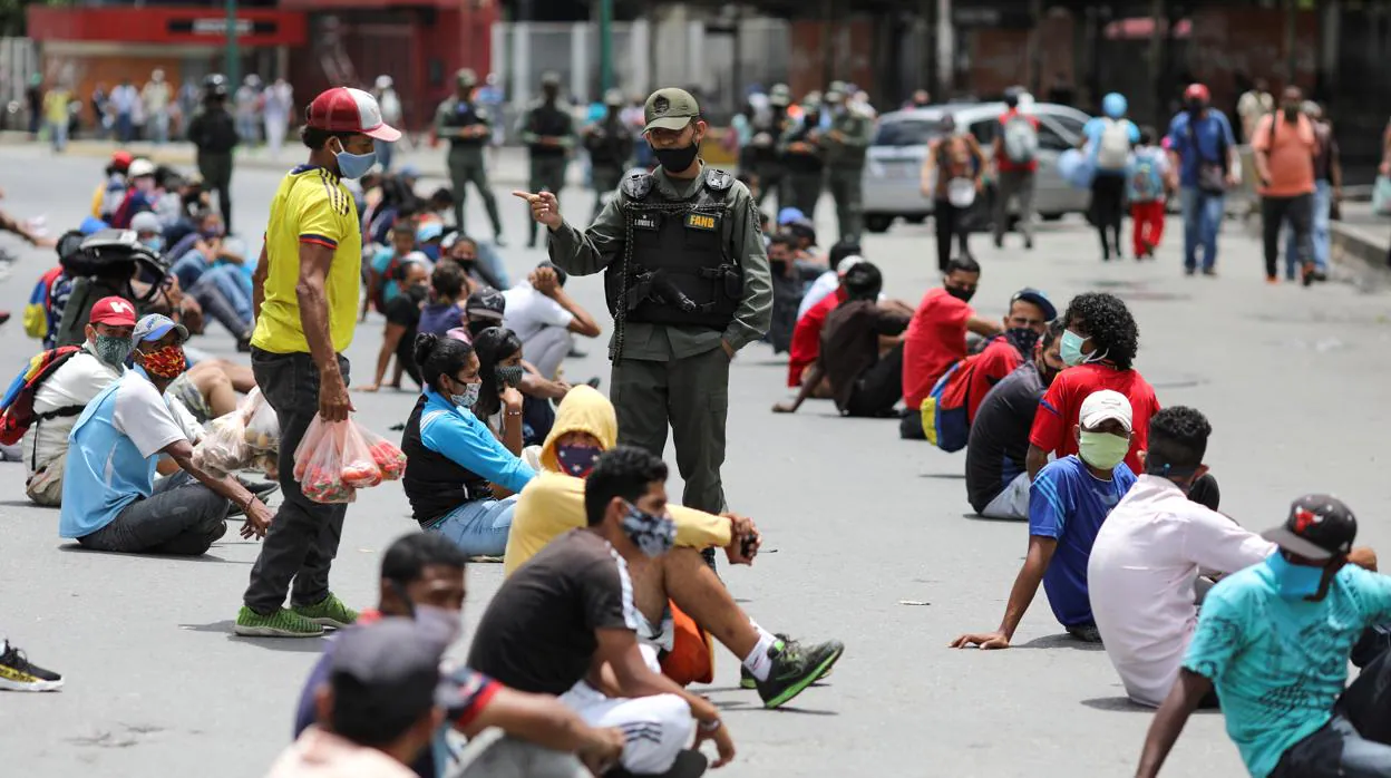 Un Guardia Nacional custodia a un grupo de personas sentadas en la mitad de la calle por no haber respetado la distancia social
