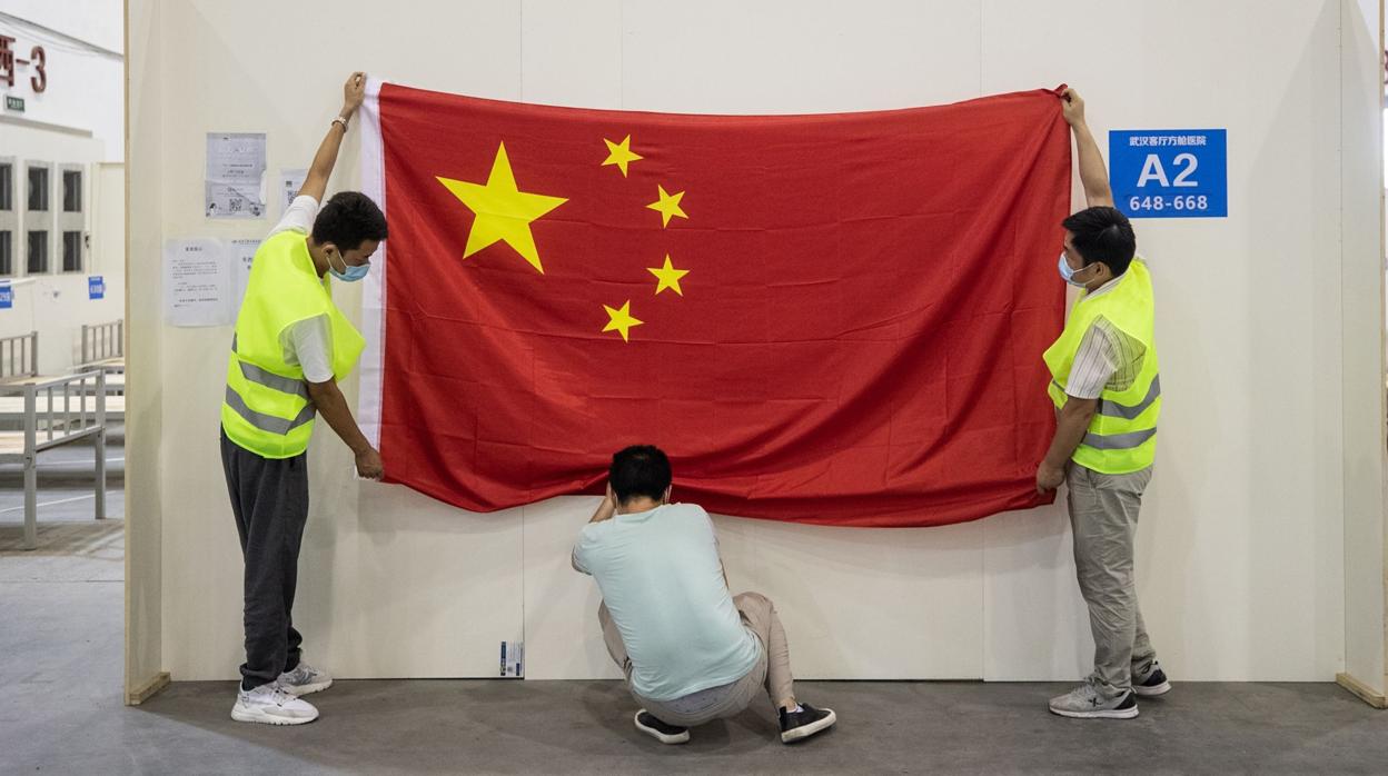 Un grupo de operarios retiran una bandera de China antes de demoler el hospital construido en Wuhan para tratar a a los afectados de coronavirus