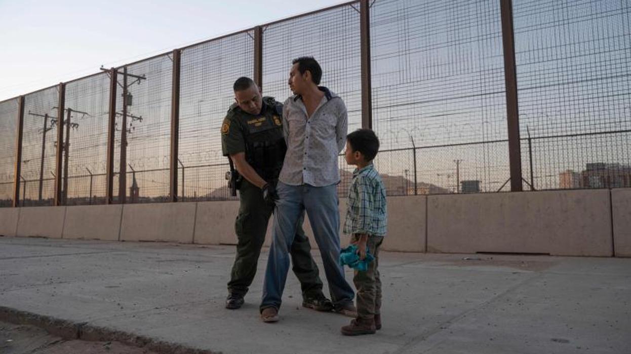 Un agente registra a un hombre junto a la frontera de EE.UU. con México ante la mirada de su hijo