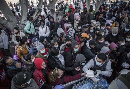 Inmigrantes esperan recibir comida en la frontera de México con EE.UU.