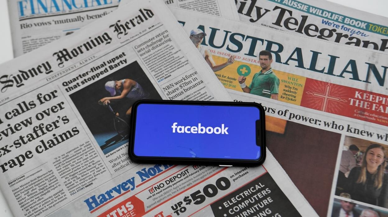 La pantalla de un móvil con el logotipo Facebook y en el fondo periódicos australianos