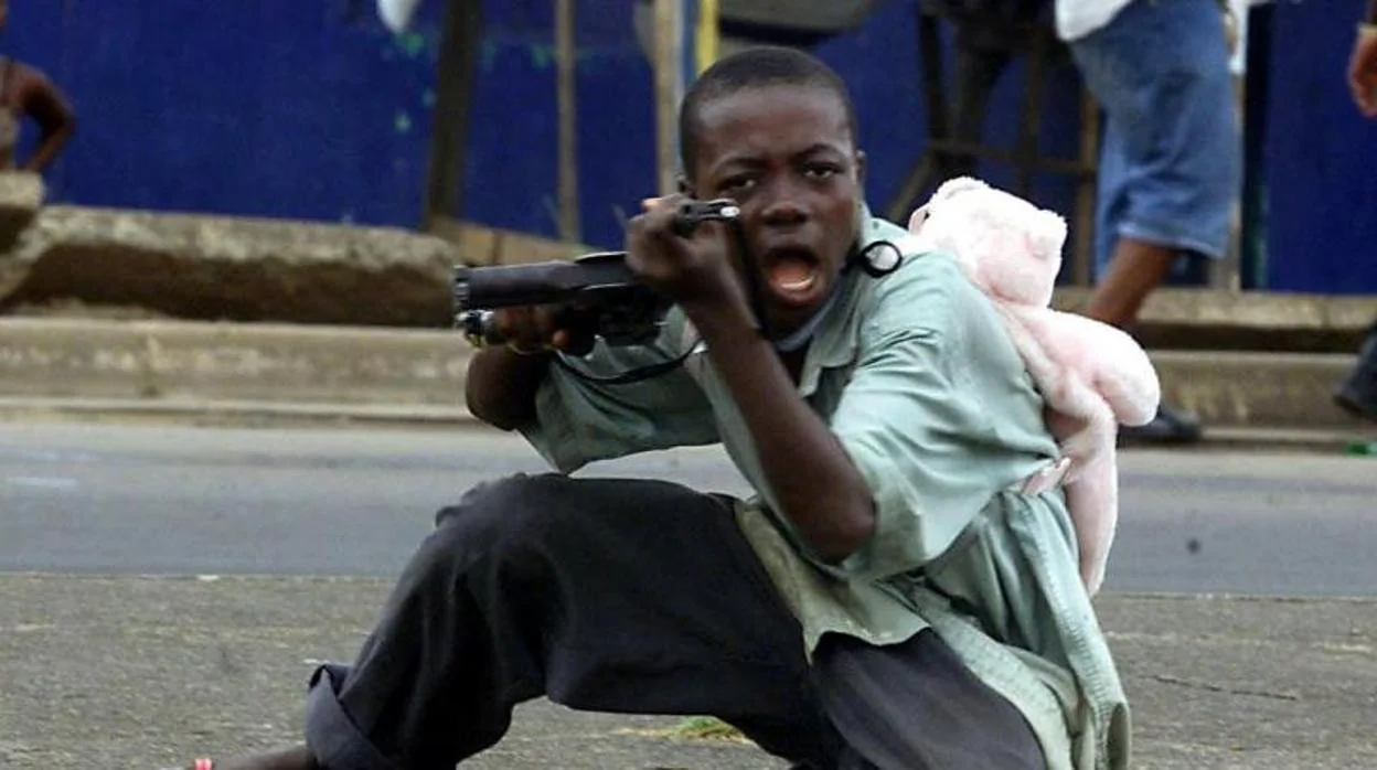 Un niño soldado con una mochila de oso de peluche apunta con su arma a un fotógrafo en Liberia en 2003