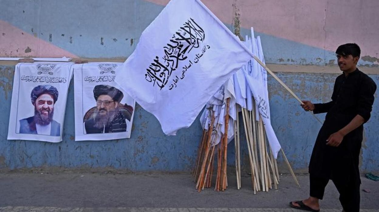 Un vendedor sujeta una bandera talibán junto a dos retratos de sus principales líderes