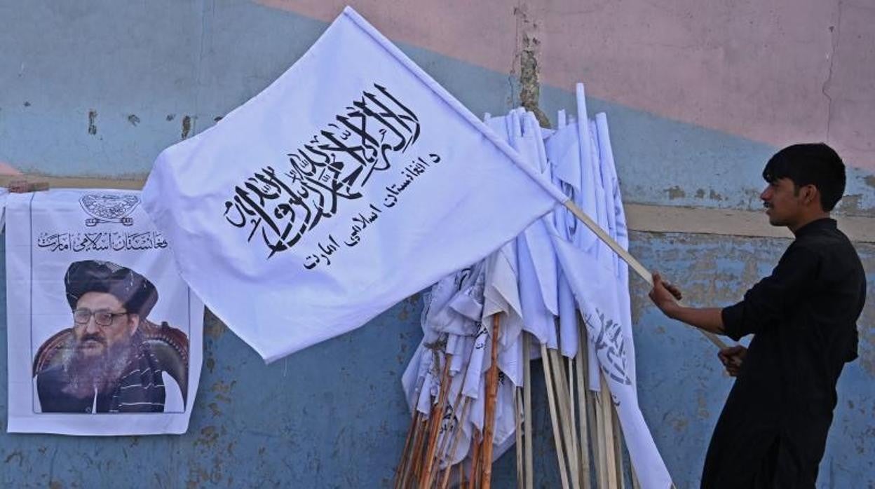 Un vendedor sostiene una bandera talibán junto a un cartel del líder talibán mulá Abdul Ghani Baradar