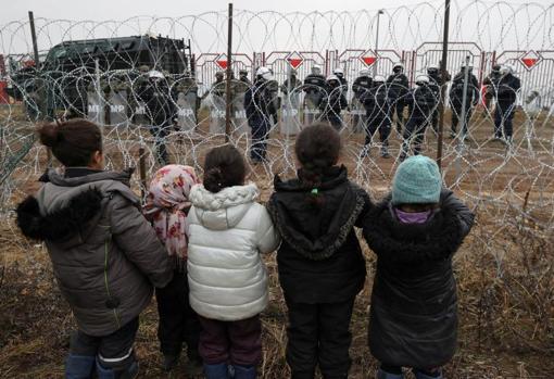 Unos niños observan a través de una alambrada a policías polacos en la frontera