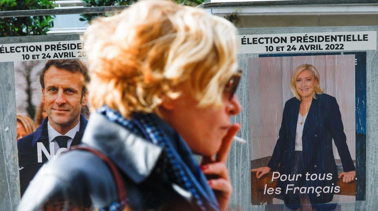 Una mujer pasa en París frente a dos carteles electorales de Macron y Le Pen