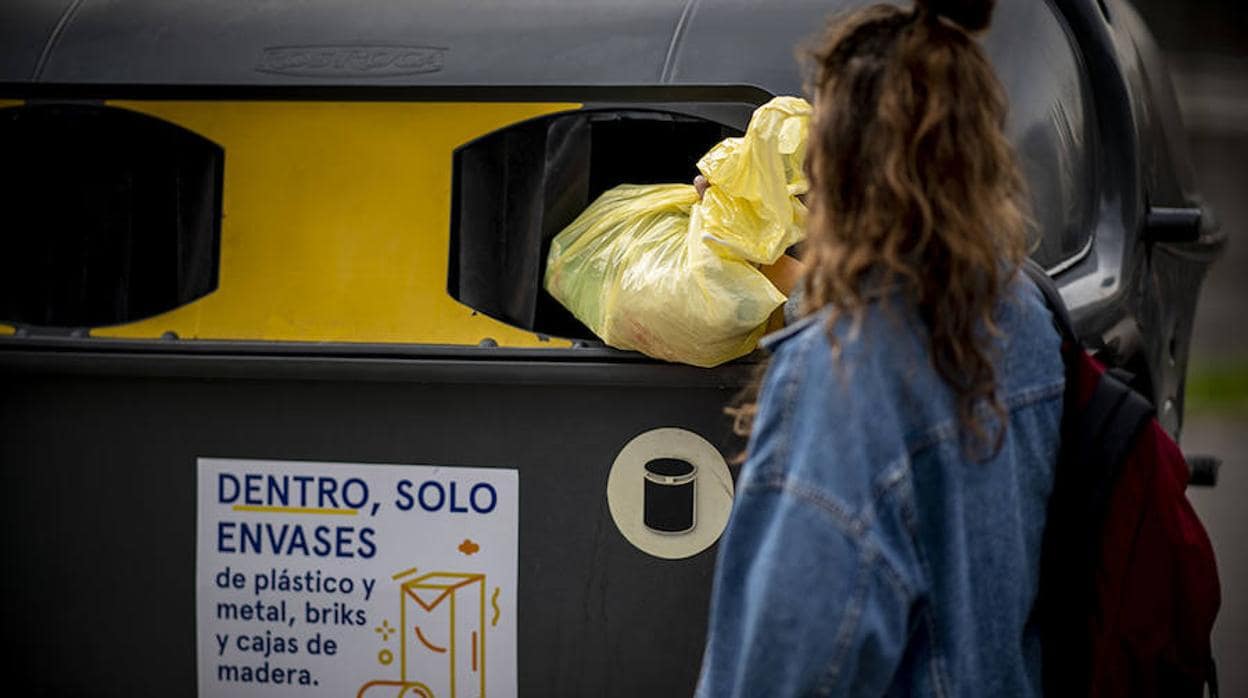 Una mujer deposita una bolsa de basura en un contenedor amarillo