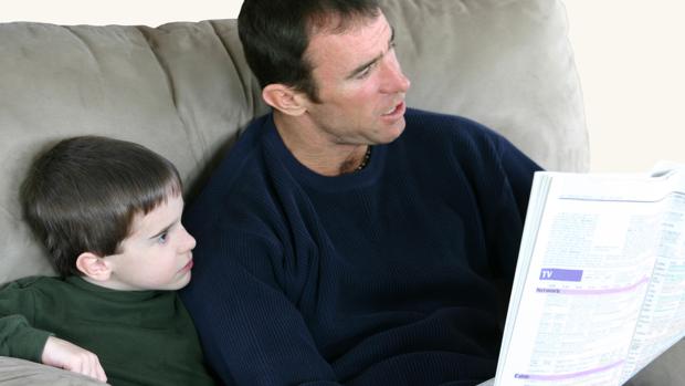 Padre e hijo leen el periódico en el sofá