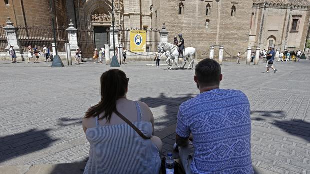 Dos turistas descansan y se resguardan del sol en una sombra por los alrededores de la Catedral de Sevilla
