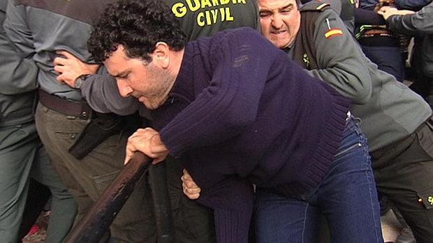 El detenido sale del coche policial mientras la Guardia Civil sujeta a los vecinos congregados en los juzgados