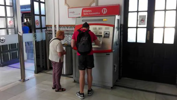 Dos usuarios sacan sus billetes de tren desde un cajero de la estación ante la falta de taquilleros
