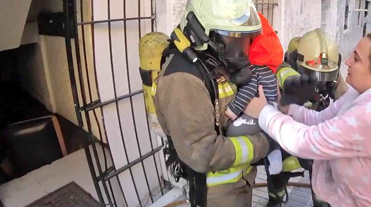 Uno de los bomberos sacan al bebé que se había quedado atrapado en el bloque con su madre