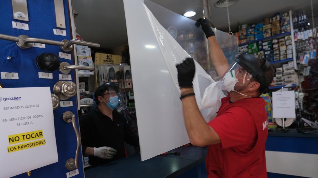 Los trabajadores de una ferretería colocan la mampara para mantener la distancia con los clientes.