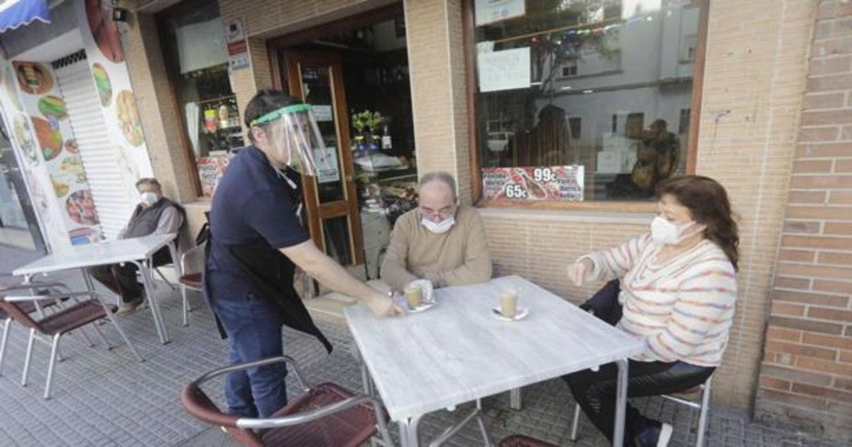 Un camarero atiende a dos clientes con todas las medidas de seguridad.