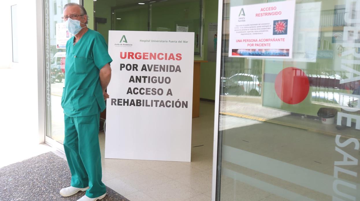 Un sanitario, en la puerta de Urgencias del Hospital Puerta del Mar junto a un cartel donde se avisa del protocolo Covid