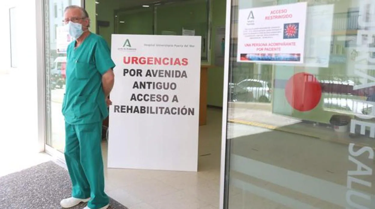 Un sanitario, en la puerta de Urgencias del Hospital Puerta del Mar junto a un cartel que informa del protocolo Covid.