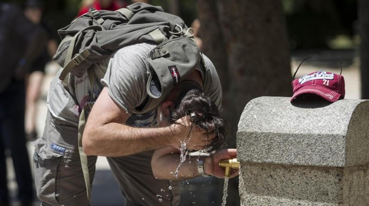 Un hombre se refresca en una fuente de la vía pública.