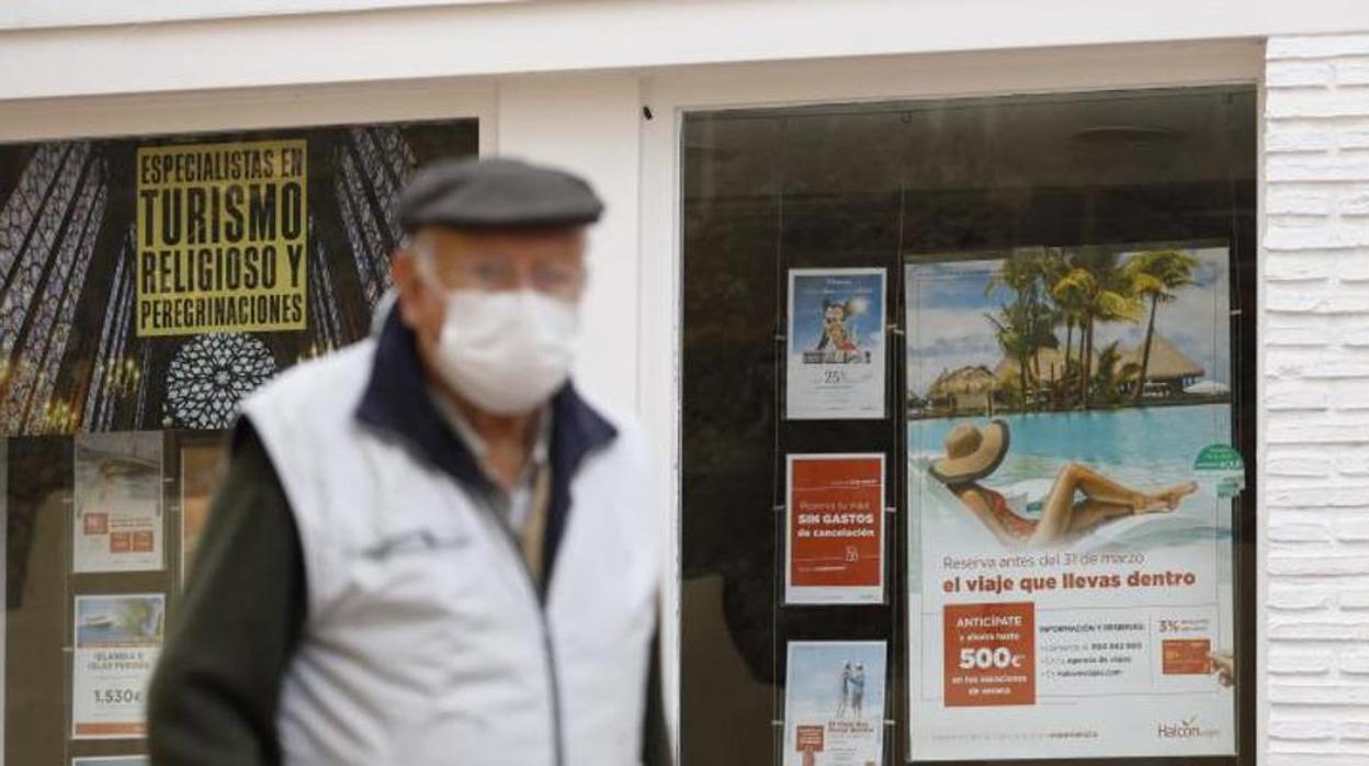 Una persona mayor pasea con mascarillas por delante de un escaparate de una agencia de viajes